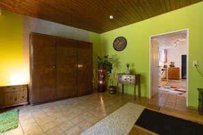 Une pièce avec une armoire en bois, un mur vert, une horloge, une plante en pot et une petite table avec des tiroirs.
