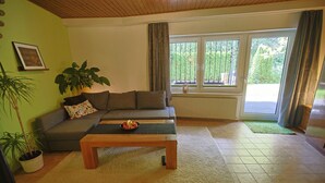 A living room with a sofa, a coffee table with fruit, a potted plant, and a view through a window.