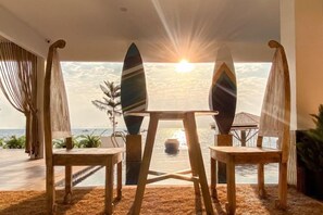 Een kamer met uitzicht op zee, twee surfplanken en een tafel met stoelen.