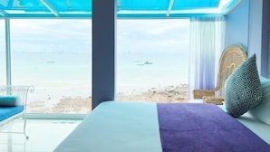 Ein Zimmer mit Bett, Sessel und Blick auf Strand und Meer.