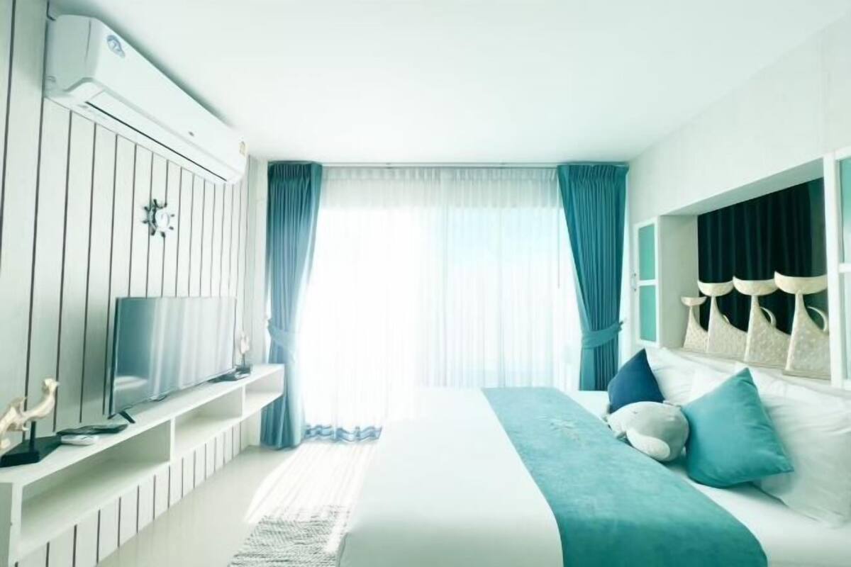 Un dormitorio con cama, televisor, aire acondicionado instalado y ventana con cortinas.