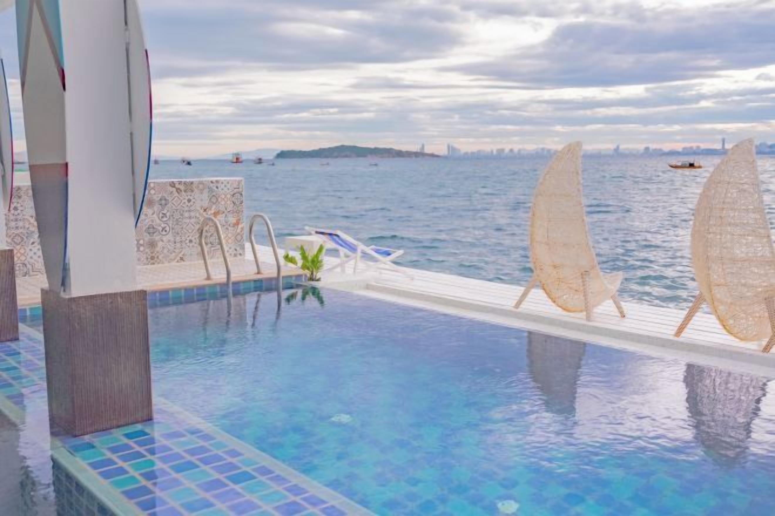 Una piscina infinita con vistas al mar, un barco y un horizonte urbano distante.
