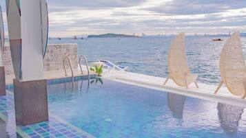 Una piscina infinita con vistas al mar, un barco y un horizonte urbano distante.