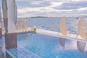 Una piscina infinita con vistas al mar, un barco y un horizonte urbano distante.