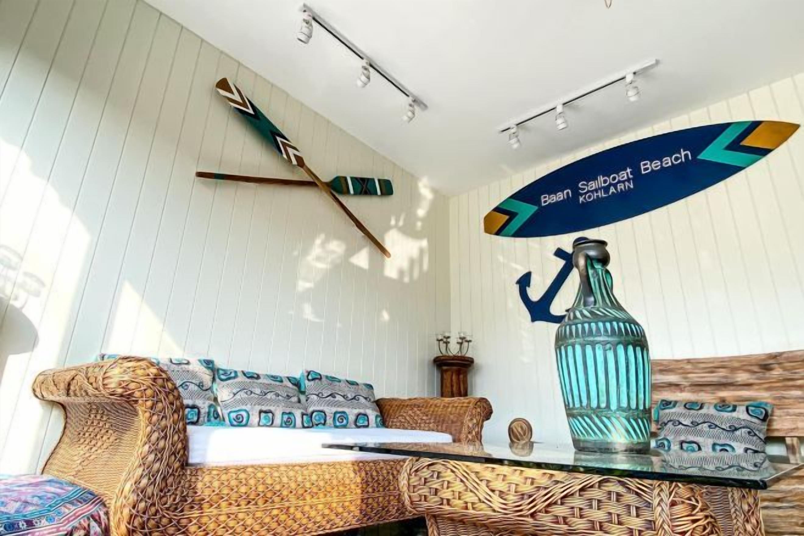 Una habitación con un sofá de mimbre, una mesa de vidrio, una botella decorativa y un letrero en la pared que indica 'Baan Soalboast Beach'.