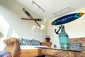Una habitación con un sofá de mimbre, una mesa de vidrio, una botella decorativa y un letrero en la pared que indica 'Baan Soalboast Beach'.