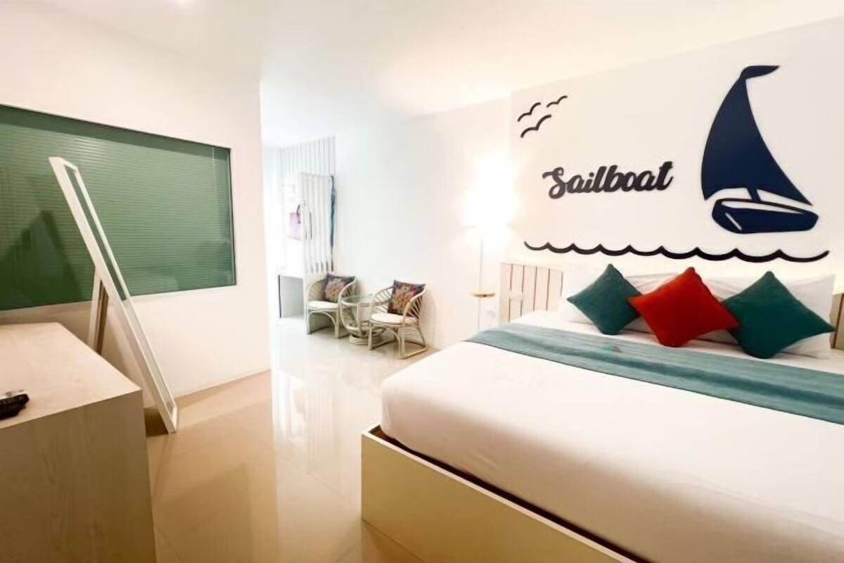 Una habitación de hotel moderna con un cuadro de un velero, una cama con almohadas, un escritorio y una silla.