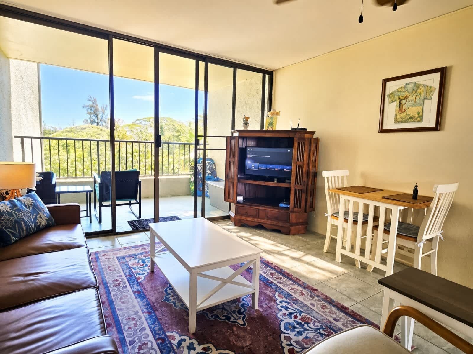 A living room with a sofa, a coffee table, a TV stand, and a balcony with a view.