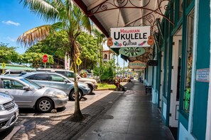 A street view with parked cars, a pedestrian crossing, and a building with a sign for 'Hawaiian Ukulele & Guitar'. - Oceanfront, Friendly Sea Turtles, Epic Snorkeling! (Hilo)