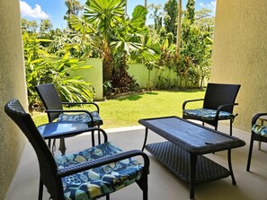 An outdoor patio area with wicker furniture and a glass table, surrounded by lush tropical plants. - Oceanfront, Friendly Sea Turtles, Epic Snorkeling! (Hilo)
