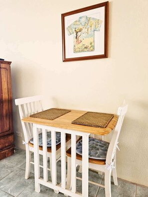 A small dining table with two chairs, a framed picture above it, and a wooden cabinet to the left. - Oceanfront, Friendly Sea Turtles, Epic Snorkeling! (Hilo)