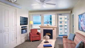 Una sala de estar con chimenea, televisor, sofá y vista al océano.