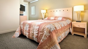 Habitación de hotel con cama, dos lámparas de noche, ventilador de techo, televisor en la pared y ventana con persianas.