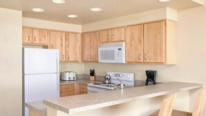 Una cocina con armarios de madera, un refrigerador, un microondas, una estufa y una cafetera.