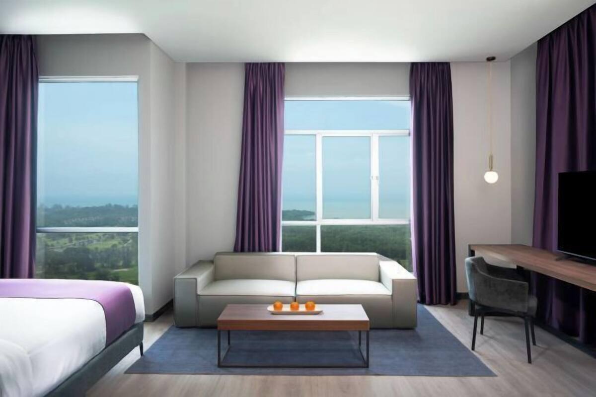 A hotel room with a bed, a sofa, a coffee table, a TV, and a large window with curtains.