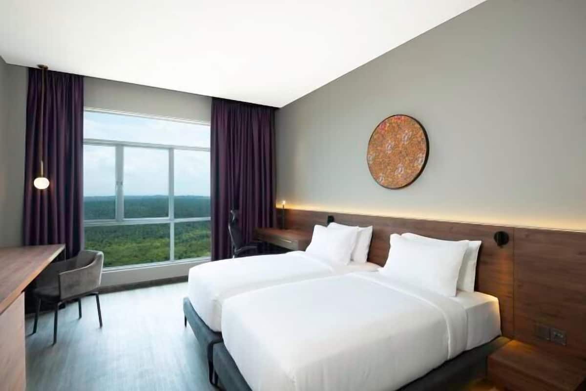 A hotel room with two beds, a desk, and a large window with curtains.