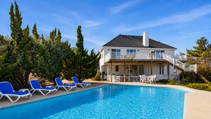 A two-story building with a swimming pool, blue lounge chairs, and a covered patio area. - Beach Retreat w/ Pool & Hot Tub (Virginia Beach)