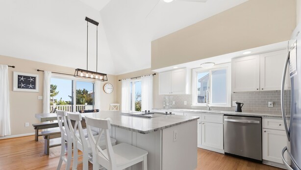 A modern kitchen with white cabinetry, a stainless steel dishwasher, and a large island with bar stools. - Beach Retreat w/ Pool & Hot Tub (Virginia Beach)