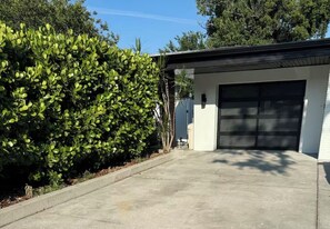 Eine Garage mit Betonauffahrt, einem weißen Gebäude und einem grünen Busch.
