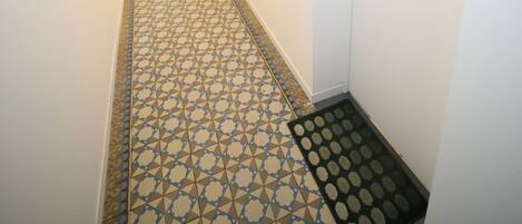 A narrow hallway with patterned floor tiles, a door with a nameplate, and a wall-mounted picture.