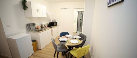 A compact kitchen with white cabinets, a small refrigerator, and a dining table set for four with chairs.
