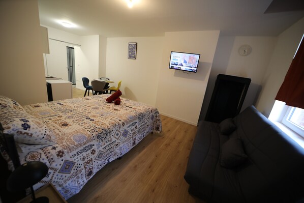Quarto com cama, escrivaninha, cadeira, televisão e janela.