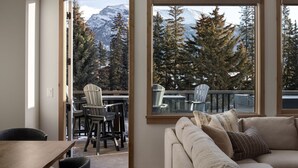 Un salón acogedor con un sofá y sillones, ventanas amplias con vistas a la montaña y una terraza de madera afuera.