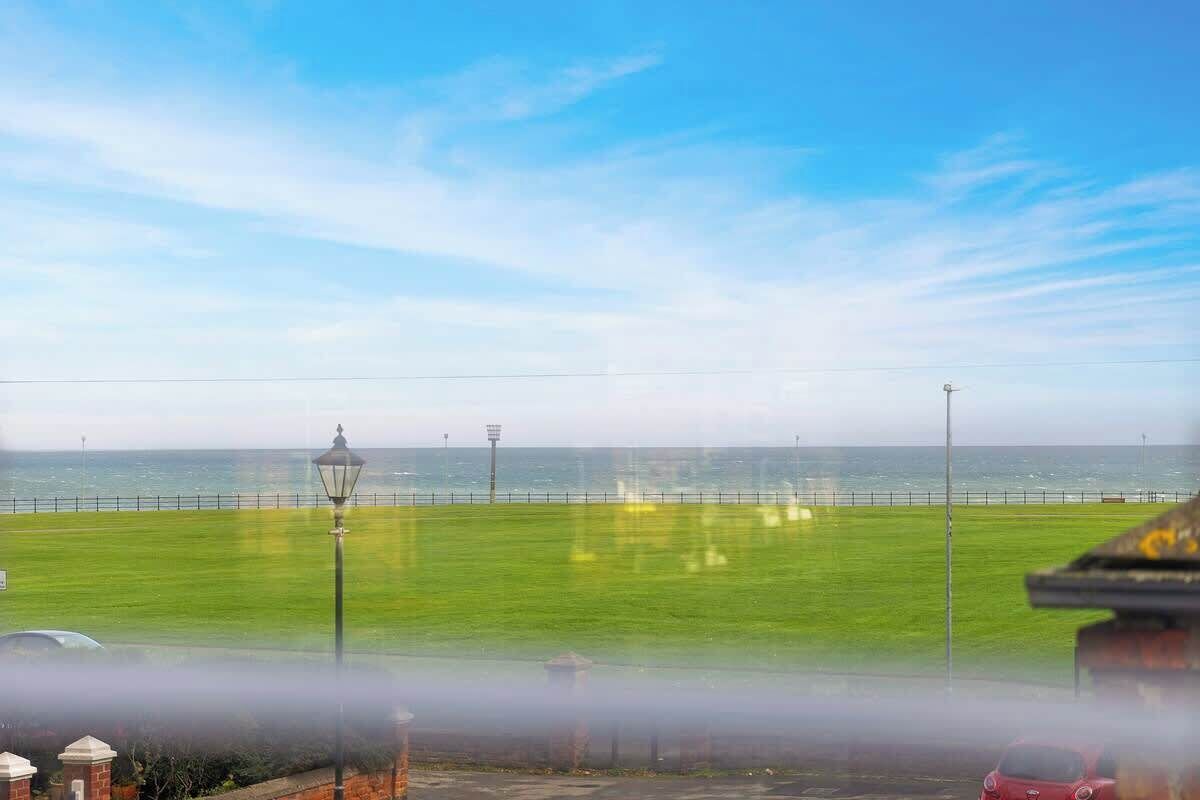 Uitzicht op de kust met een grasveld, een lantaarnpaal en een rode auto.