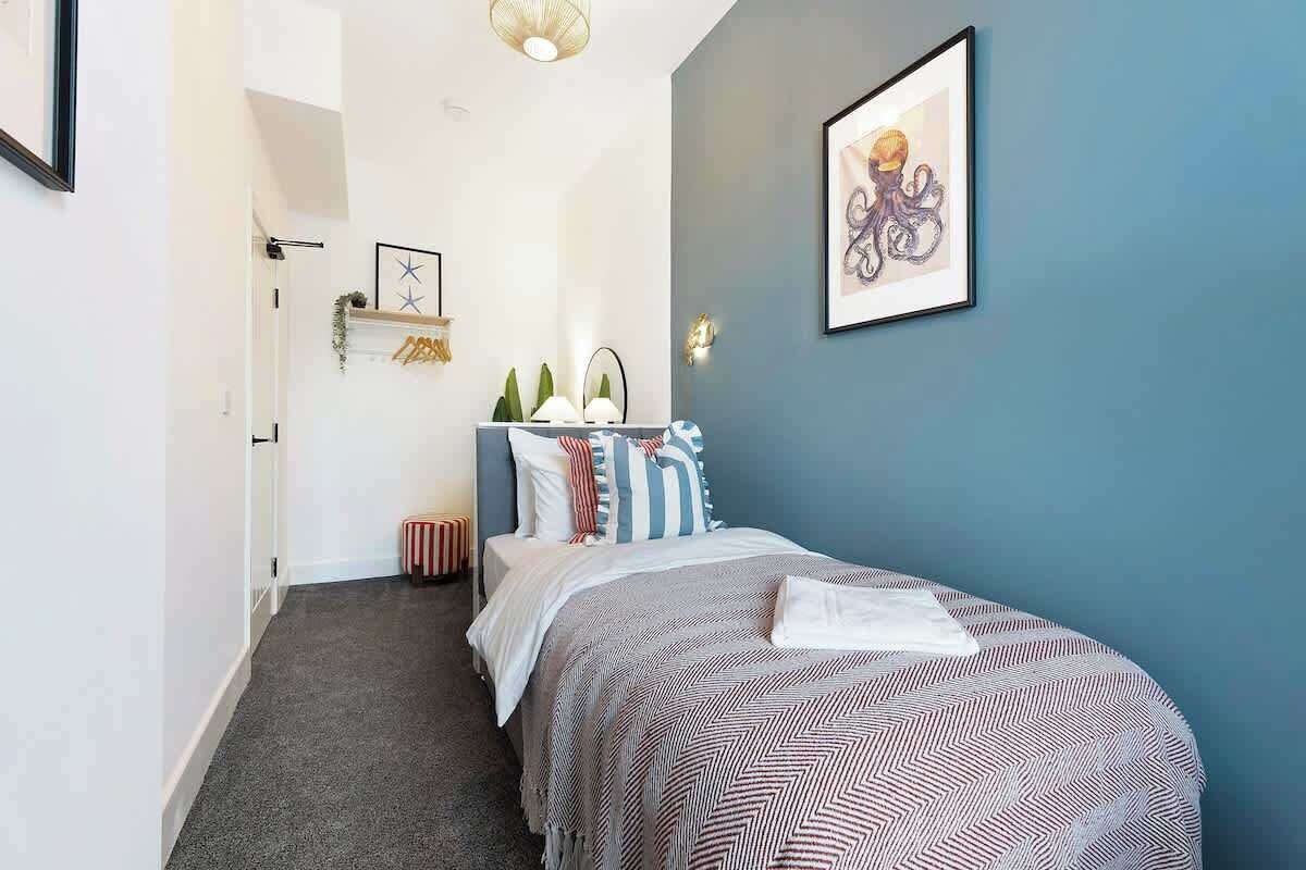 Een slaapkamer met een bed, nachtkastje, lamp en een ingelijst schilderij aan de muur.