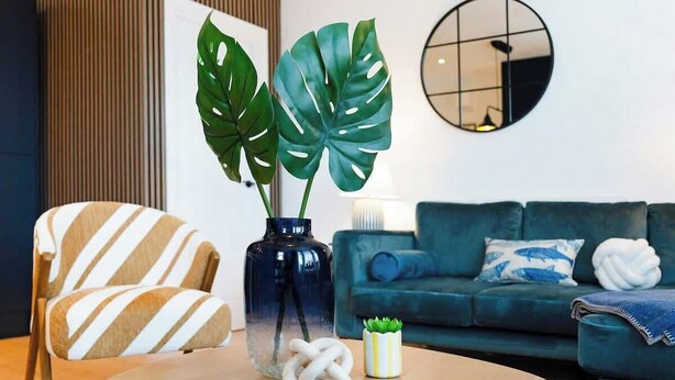 Una sala moderna con una mesa de centro redonda de madera, un sillón a rayas y un sofá azul con cojines decorativos.
