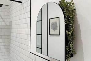 Un baño con paredes de azulejos blancos, un espejo y un cuadro enmarcado.