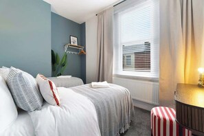Un dormitorio con dos camas, una mesita de noche, un radiador y una ventana con persianas.