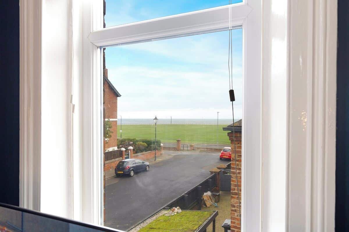 A view through a window of a residential street with a brick house, a car, and a green field in the distance.