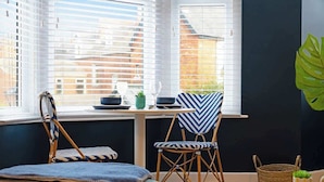 Una habitación con ventana, dos sillones de mimbre, una mesita con una planta y un adorno grande con hojas verdes.