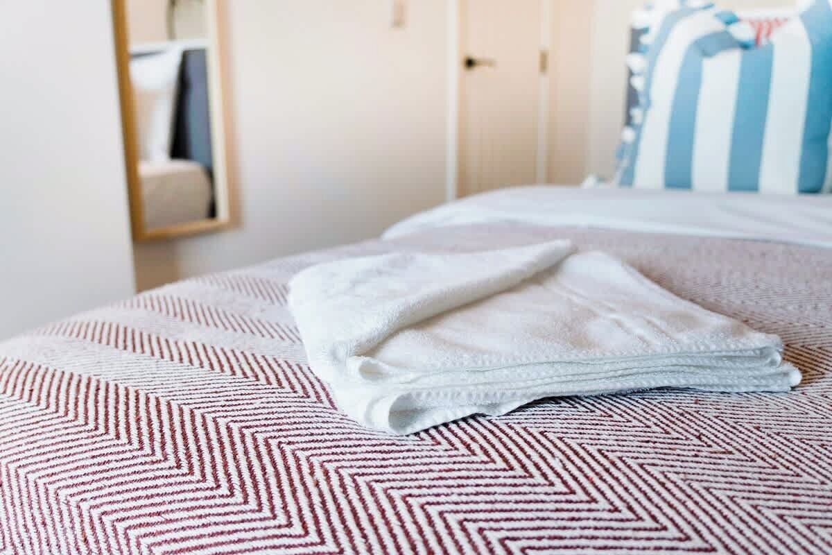 Ein ordentlich gemachtes Bett mit einer gemusterten Tagesdecke, einem gefalteten weißen Handtuch und einem gestreiften Kopfkissen.
