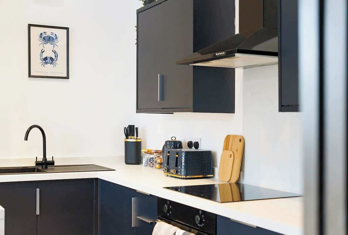 A modern kitchen with dark cabinets, a stainless steel sink, a toaster, and a wooden cutting board.