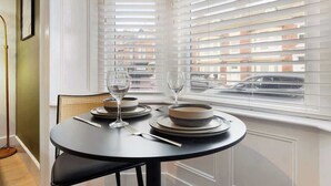 A dining table set with plates, glasses, and cutlery in a room with white walls and a window with blinds. - Hartlepool Retreat | 2BR | Sleeps 4 | by Stay With Us (Hartlepool)