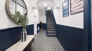 A hallway with a patterned floor, a round mirror, and framed artwork on the walls. - Hartlepool Retreat | 2BR | Sleeps 4 | by Stay With Us (Hartlepool)