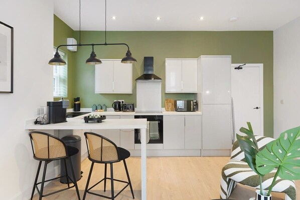 Una cocina moderna con armarios blancos, una encimera blanca y dos taburetes negros.