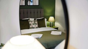 A hotel room with a bed, pillows, a nightstand with a lamp, and a wall with framed pictures. - Hartlepool Retreat | 2BR | Sleeps 4 | by Stay With Us (Hartlepool)