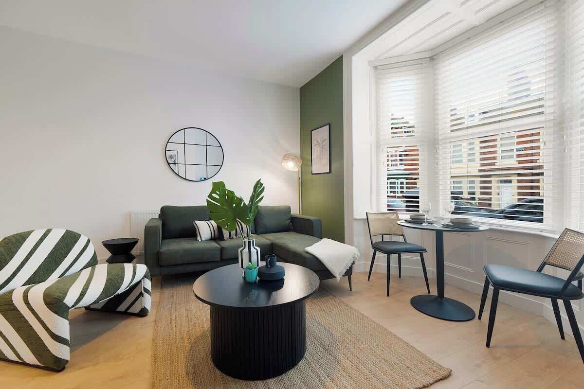 A modern living room with a sofa, chairs, a coffee table, and a window with blinds.