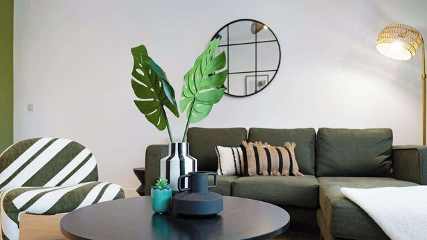 A modern living room with a round coffee table, striped armchairs, a green sofa, a potted plant, and a wall-mounted mirror. - Hartlepool Retreat | 2BR | Sleeps 4 | by Stay With Us (Hartlepool)