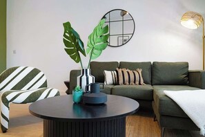 Una sala de estar moderna con una mesa redonda, sillones a rayas, un sofá verde, una planta en maceta y un espejo montado en la pared.
