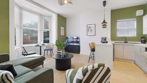 A modern living room with a sofa, a coffee table, and a TV. There is a kitchen area with a sink and cabinets. - Hartlepool Retreat | 2BR | Sleeps 4 | by Stay With Us (Hartlepool)