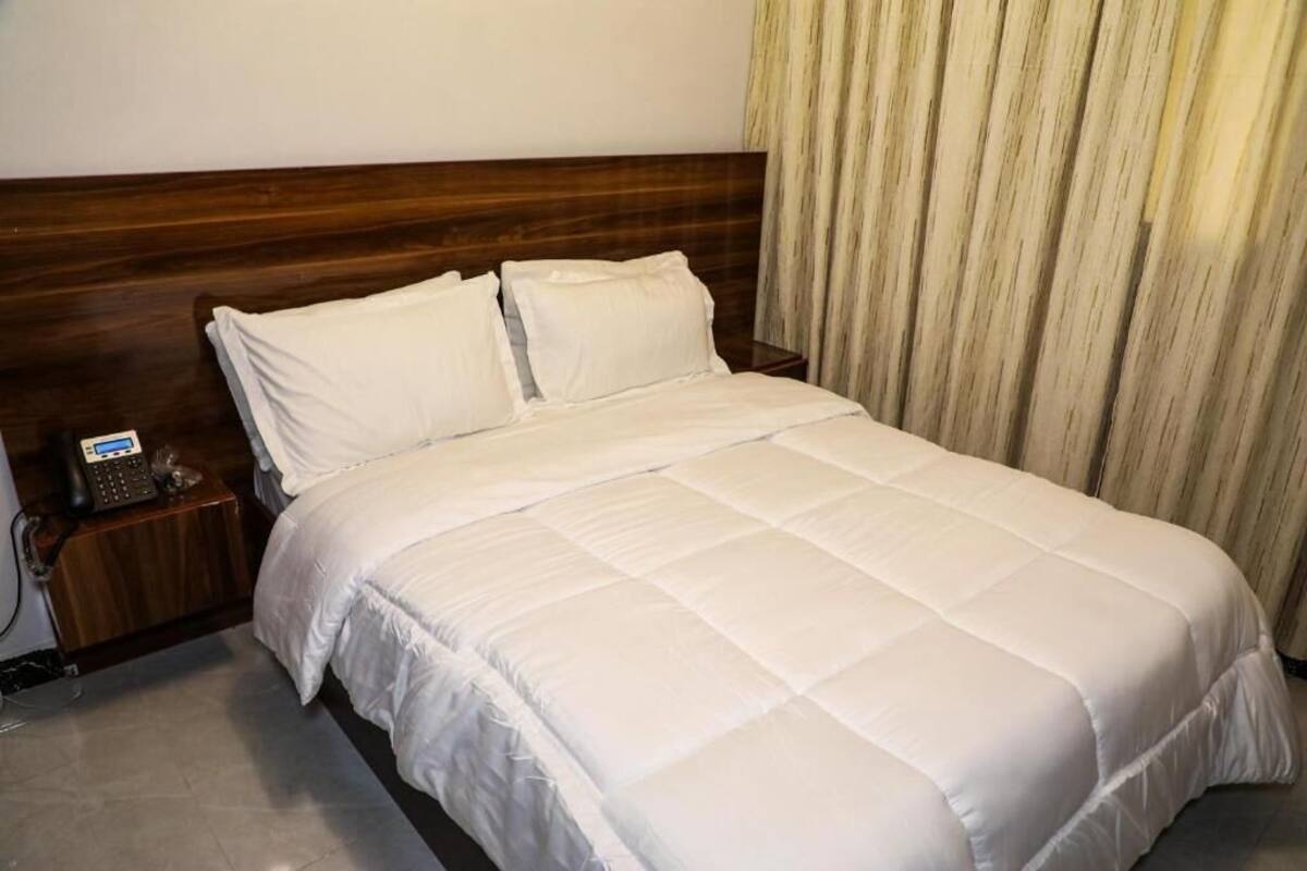 A neatly made bed with white bedding, a wooden headboard, and a bedside telephone.