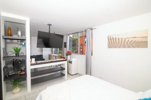 Ein modernes Hotelzimmer mit einem Bett, einem Schreibtisch mit Computer, einem Fernseher und einem Fenster mit Blick auf Gebäude.