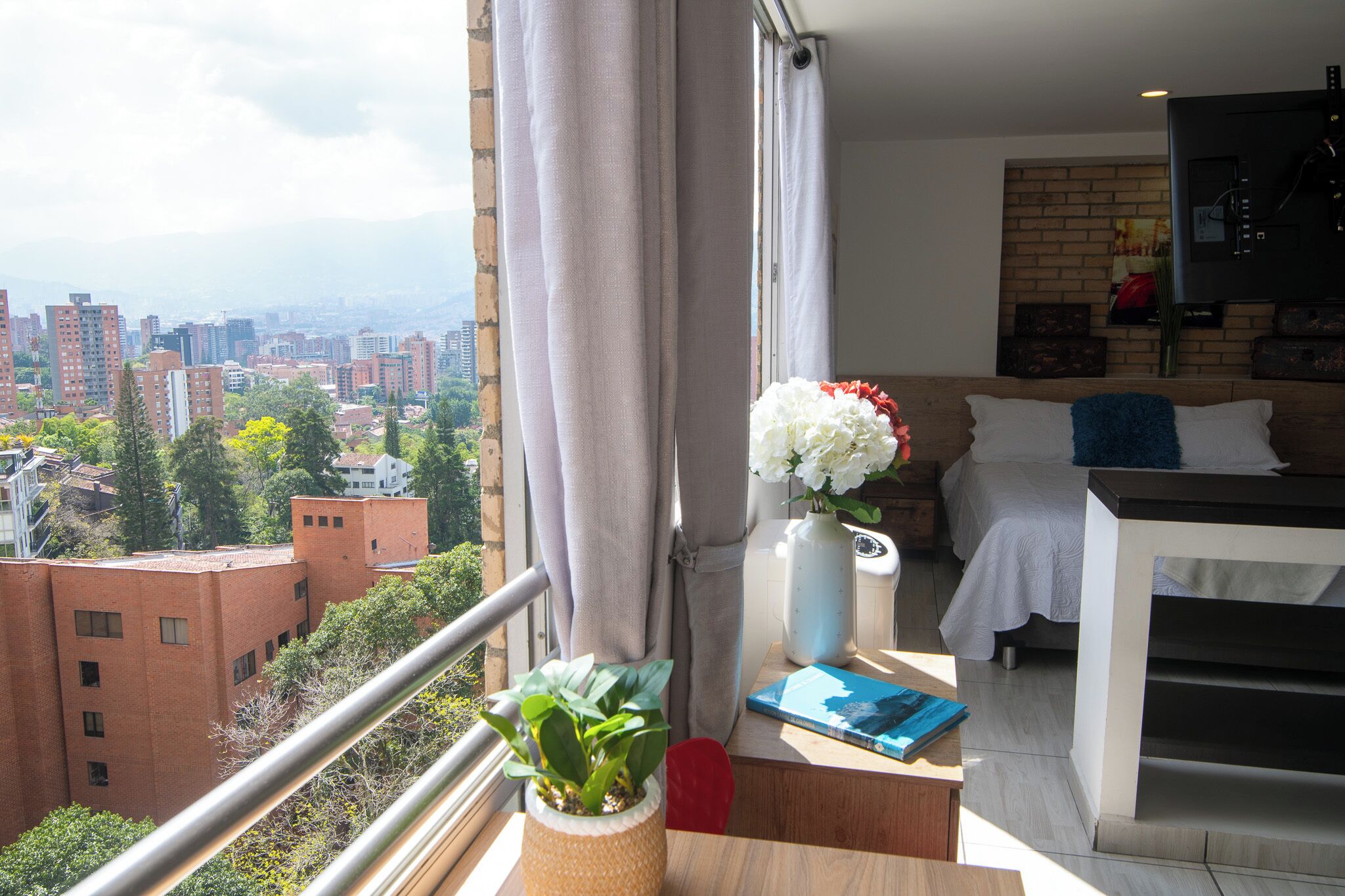 A modern room with a balcony, a bed, a TV, and a view of a cityscape.