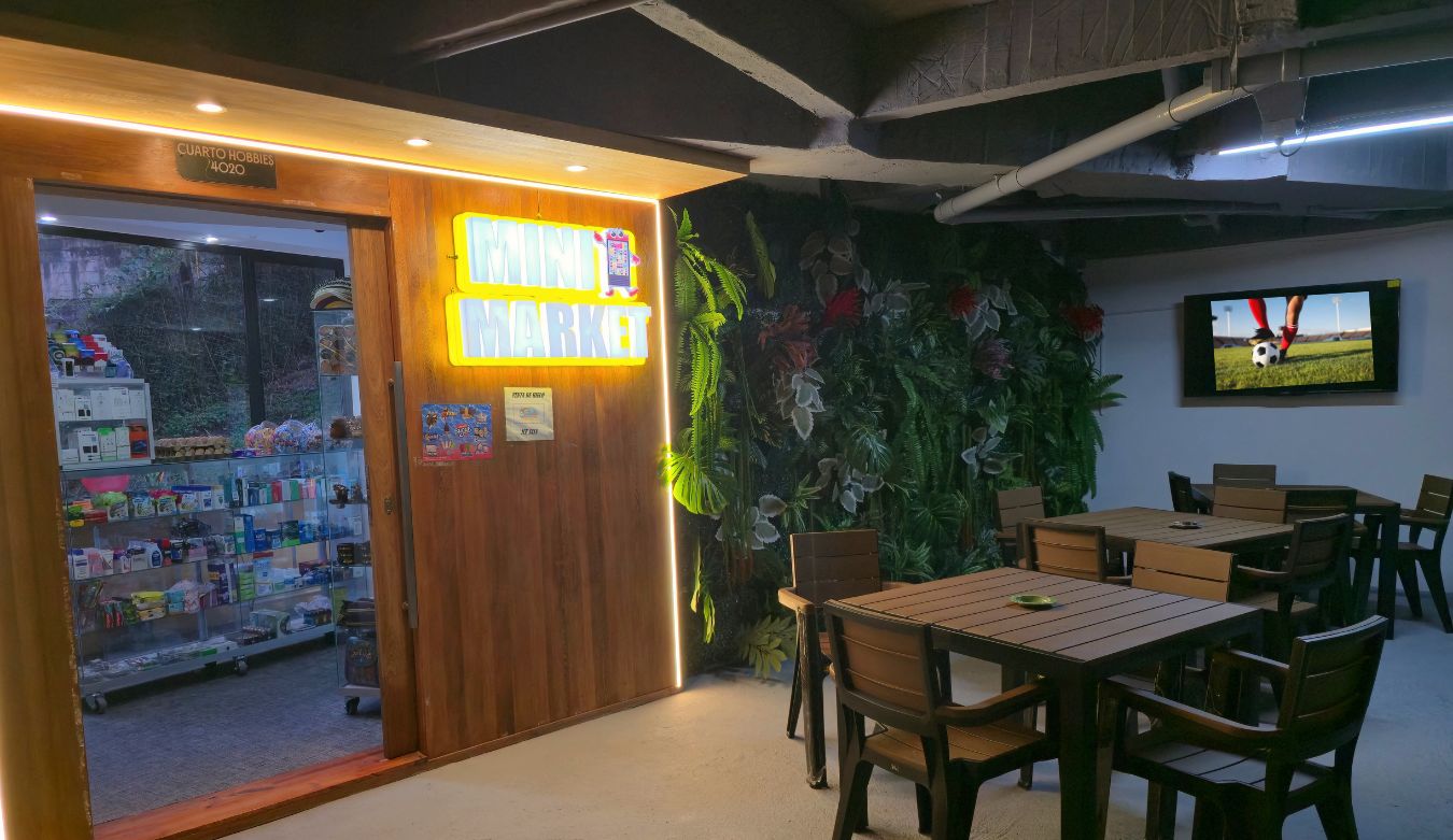 A room with a wooden door labeled "MINI MARKET," a television, and a dining area with chairs and tables.