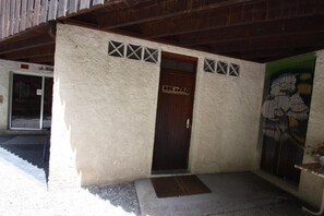 A building with a textured exterior, a wooden door, and a small entrance area with a mat. - 300m from ski slopes, view mountain, balcony, tv, 21m², Pra Loup (Pra Loup)