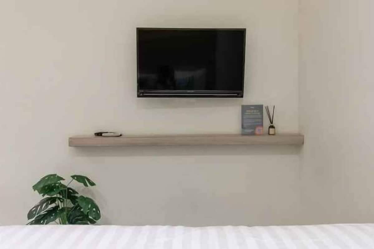 A television mounted on a wall above a wooden shelf with a plant and a small decorative item.